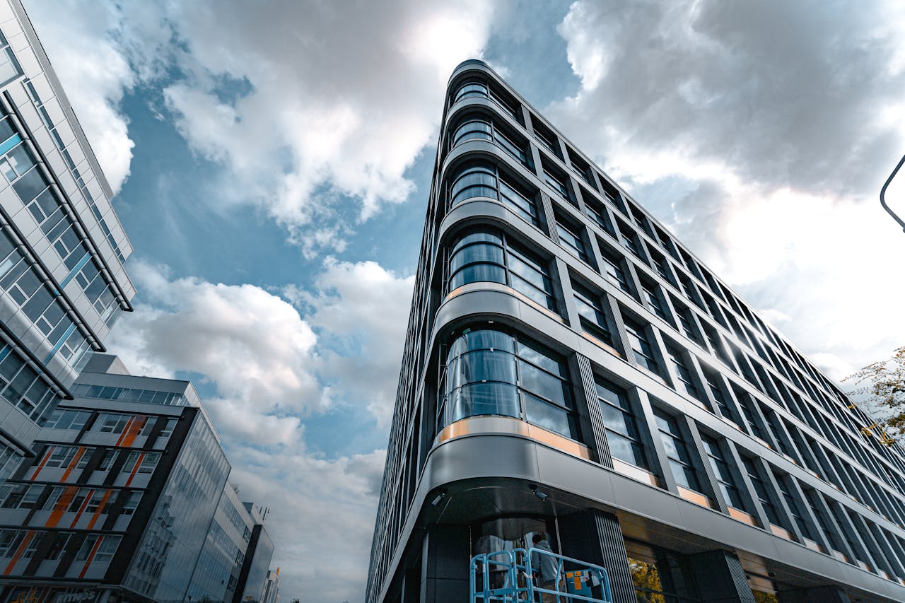 Services Low angle view of a modern office building with a sleek glass facade against a cloudy sky.
